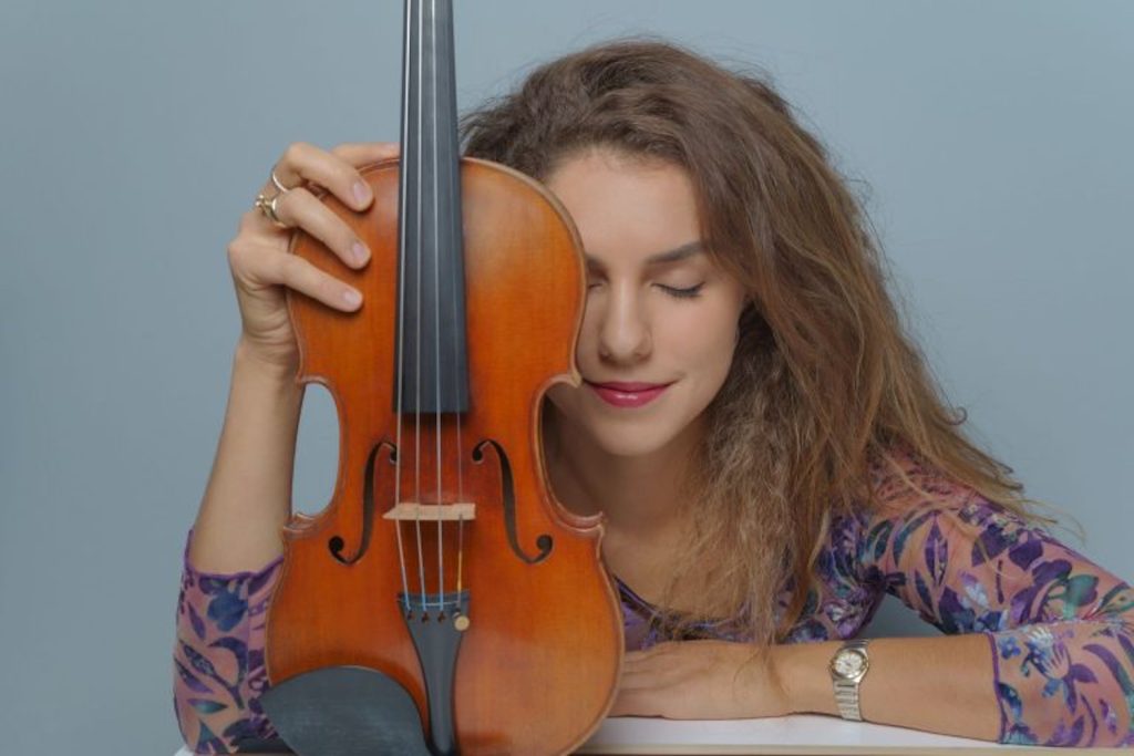 Sabina Bakholdina stützt sich mit dem linken Arm auf und hält im linken ihre Geige. Sie hat die Augen geschlossen. (KLANGherbst) © Sabina Bakholdina