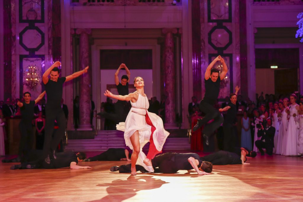 Tänzer*innen beim Kaffeesiederball 2023. In der Mitte eine Frau im weißen Kleid, am Boden und hinter ihr Männer in schwarzer Bekleidung
