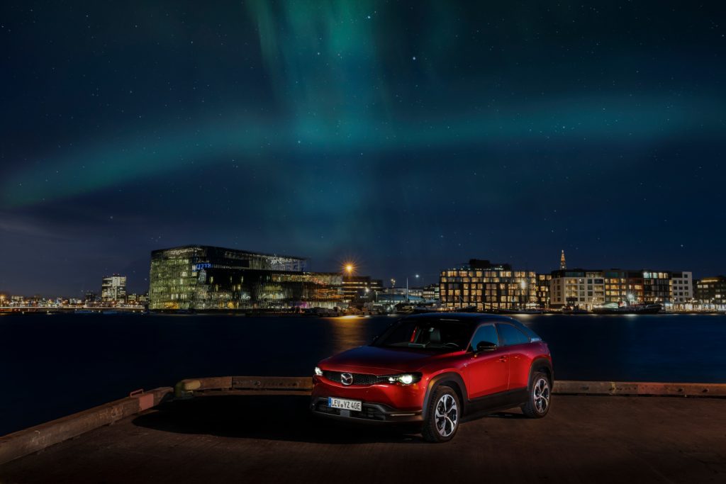 Roter Mazda MX-30 R-EV, in Hintergrund Lichter aus der Stadt