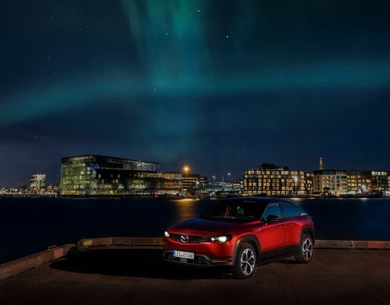 Roter Mazda MX-30 R-EV, in Hintergrund Lichter aus der Stadt