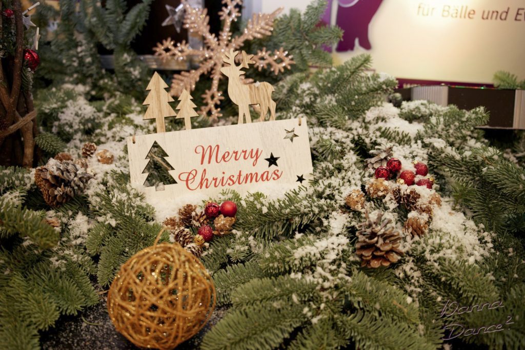Weihnachtsdeko beim Weihnachtsball. FalscherSchnee, Holz-täfelchen mit "Merry Christmas"-Aufschrift, Tannenzapfen, drapiert auf Ästen eines Nadelbaums