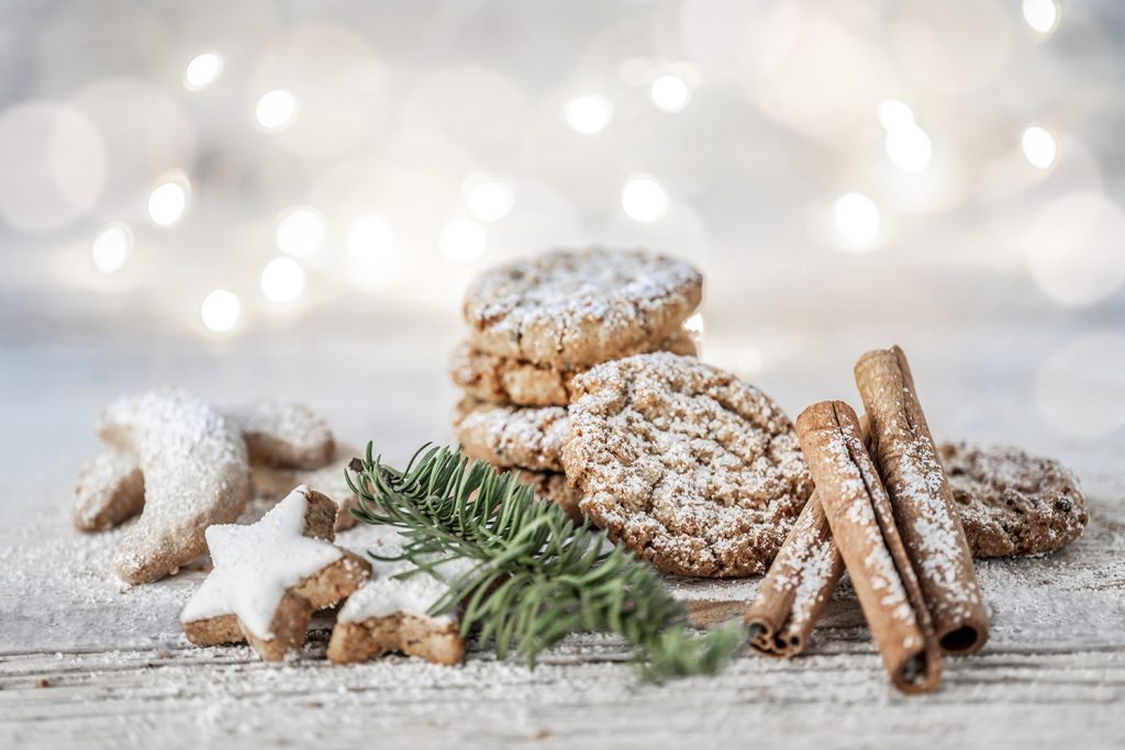 Kochen mit Christina: Zimtsterne, Vanillekipferl und Weihnachtskekse mit Tannenzweig und Zimtstangen vor weißem Hintergrund auf hellem Holz.