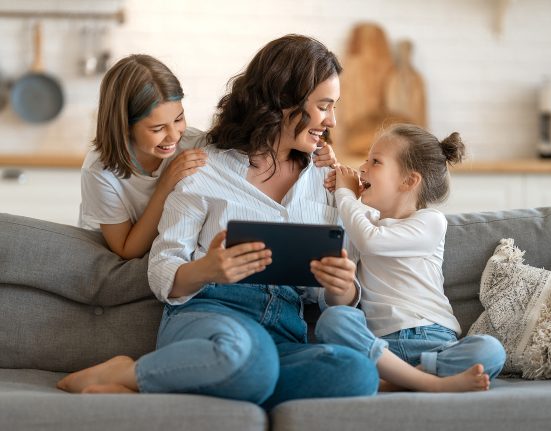 Medienkompetenz bei Kindern fördern: Mutter mit Tablet in der Hand und zwei Töchtern auf der Couch.