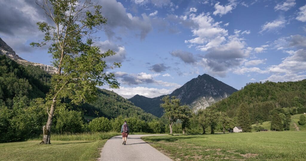 Eine Frau ist auf dem Weg der Achtsamkeit unterwegs. Sie ist von einer eindruckvollen Natur umgeben und die Wolken am blauen Himmel schaffen eine mystische Atmosphäre.