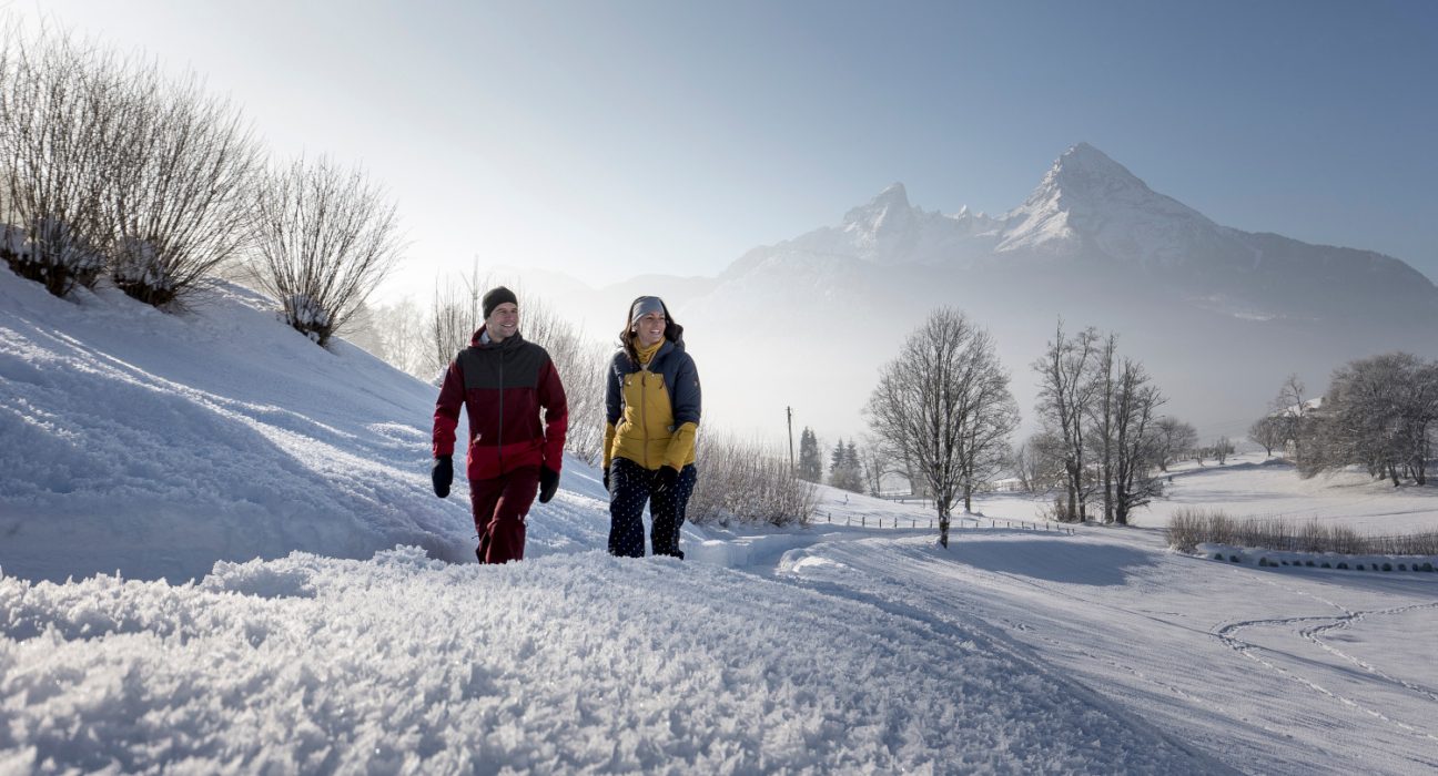 Paar bei Winterwanderung bei Schnee und Sonne vor Kulisse des Berges Watzmann in Berchtesgaden.