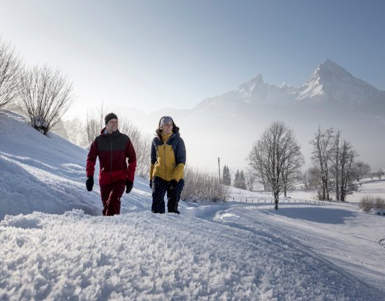 Paar bei Winterwanderung bei Schnee und Sonne vor Kulisse des Berges Watzmann in Berchtesgaden.