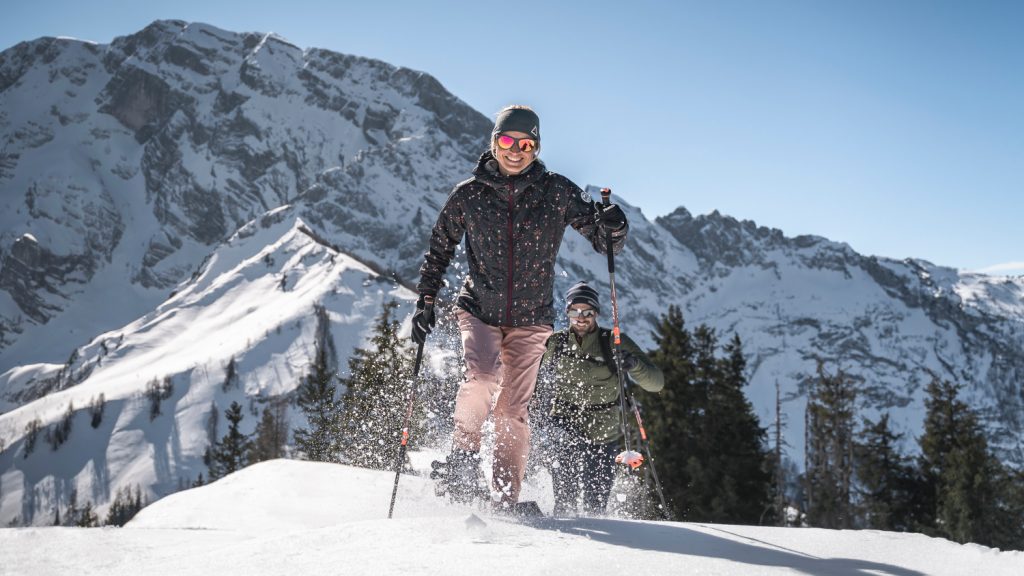 Paar beim Schneeschuhwandern bei Sonnenschein vor Bergkulisse von Berchtesgaden