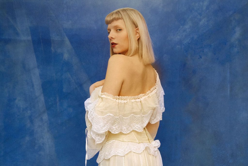 Promobild: Aurora in weißem Kleid vor blauem Hintergrund
