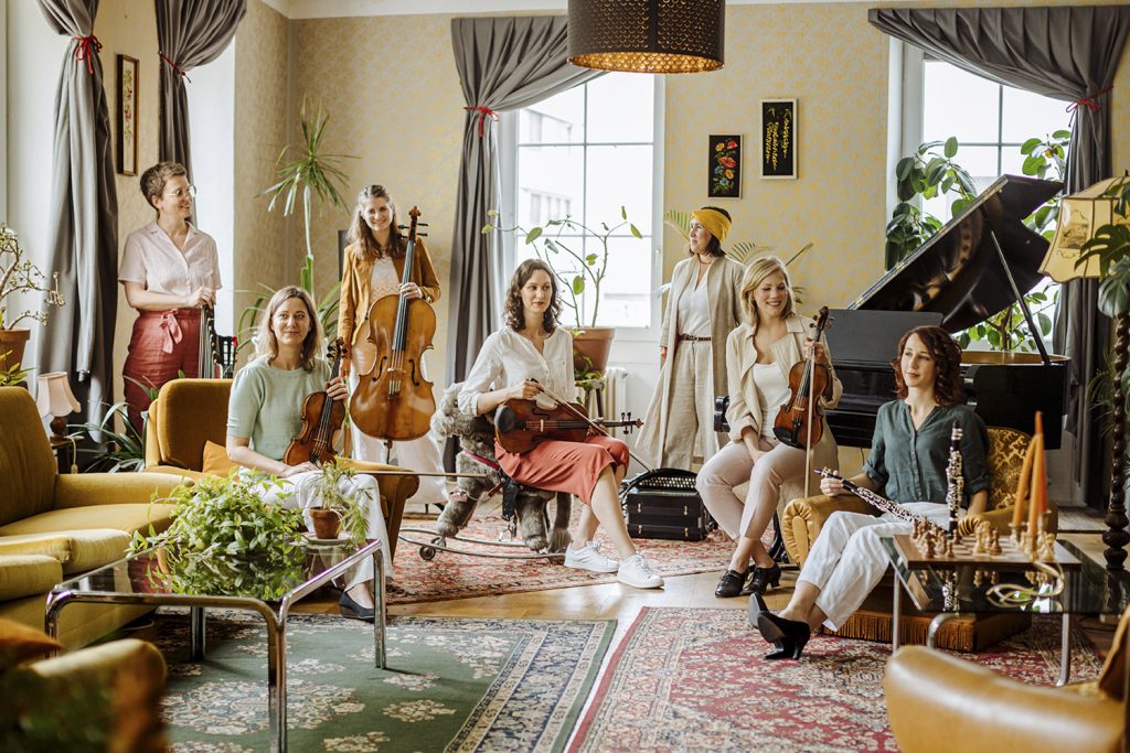 Mitglieder der Gruppe Divinerinnen sitzen mit ihren Instrumenten in der Hand in einem hellen Raum voller Deko