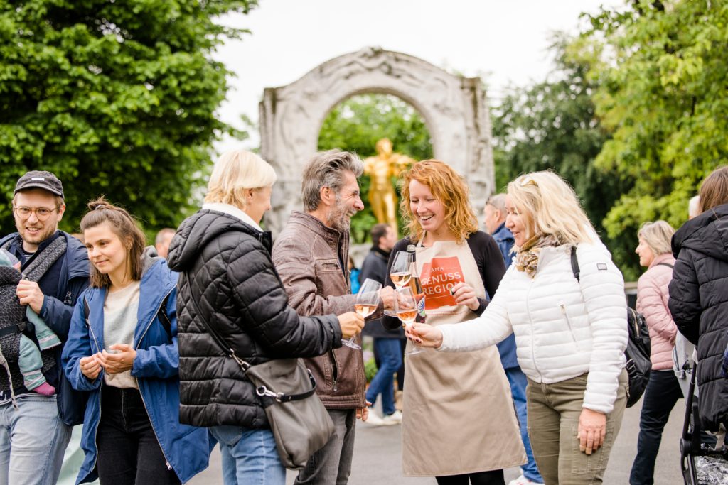 Eine Gruppe von Menschen steht im Wiener Stadtpark und stößt mit Weingläsern an.