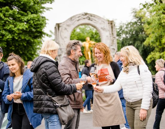 Eine Gruppe von Menschen steht im Wiener Stadtpark und stößt mit Weingläsern an.