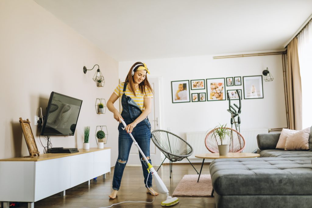 Frau in Latzhose wischt den Boden in einer minimalistisch eingerichteten, hellen Wohnung