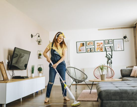 Frau in Latzhose wischt den Boden in einer minimalistisch eingerichteten, hellen Wohnung