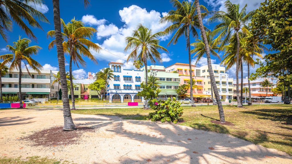 Farbenfrohe Häuserfront im Art Déco Stil hinter Palmen und vor blauem Himmel