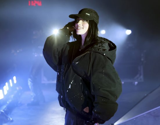 Die Sängerin Billie Eilish steht mit einem Mikrofon auf einer Bühne.