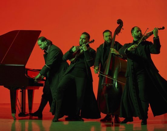 Die vier Mitglieder des Janoska Ensembles spielen ihre Instrumente. Sie sind schwarz gekleidet, die Instrumente allesamt sehr dunkelfarbig. Der Hintergrund ist knallrot.