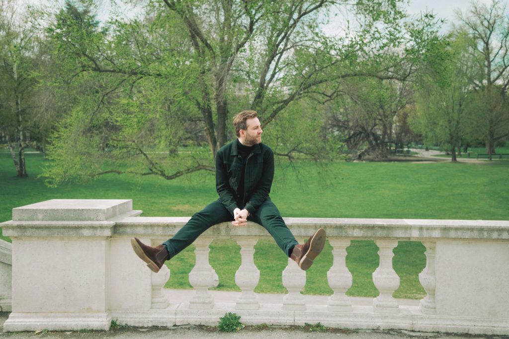 Sänger Josh auf einer Steinermauer in einem Park mit gespreizten Beinen