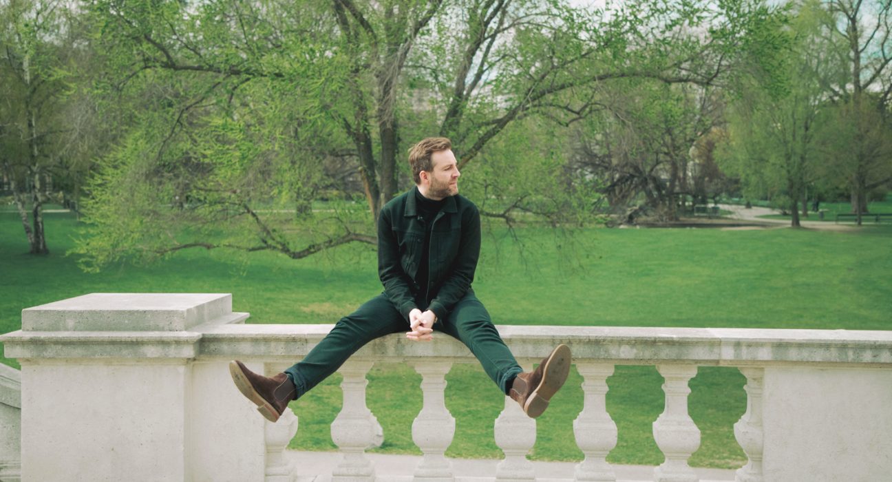Sänger Josh auf einer Steinermauer in einem Park mit gespreizten Beinen
