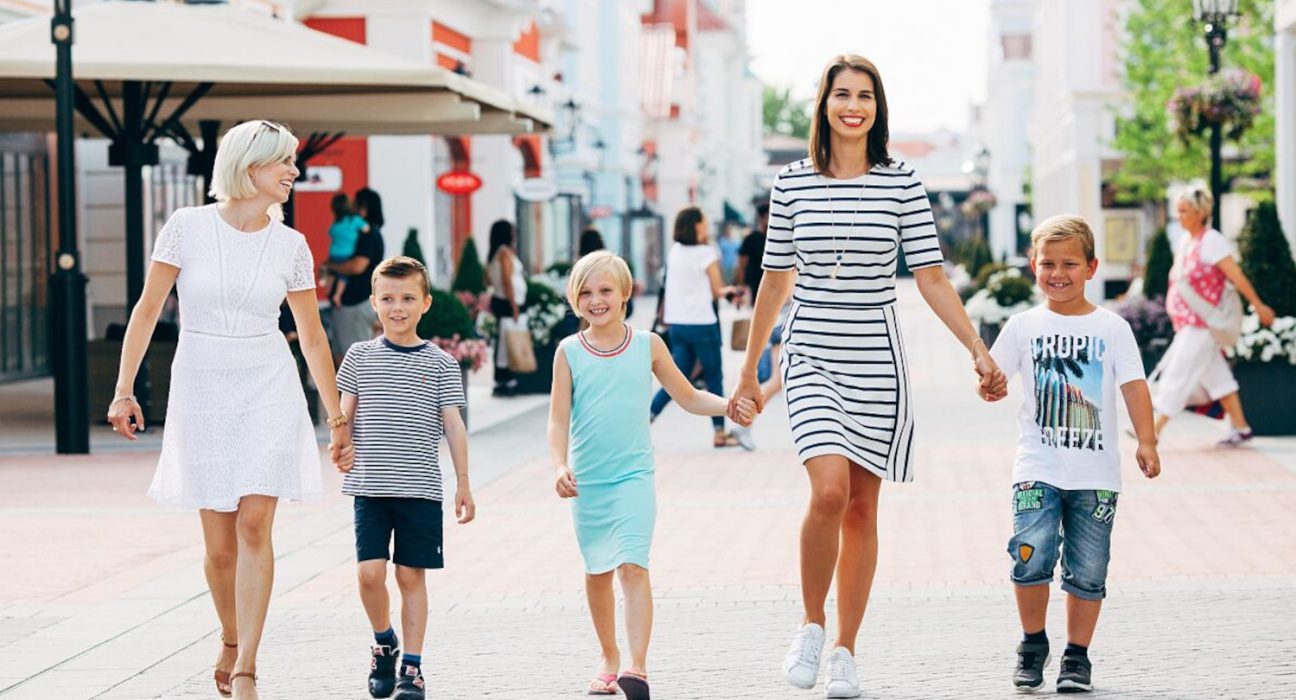 Zwei Frauen gehen mit drei Kindern durch eine Einkaufsstraße.