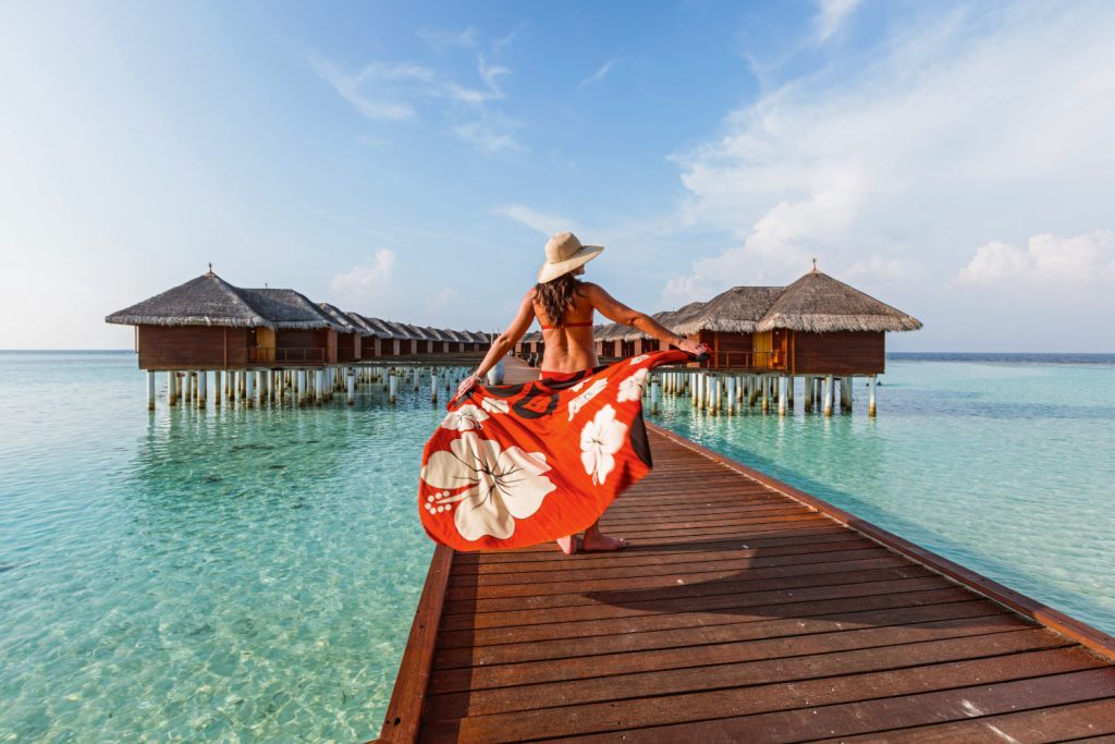 Frau in rotem Kleid und mit Hut auf einem Steg auf den Malediven