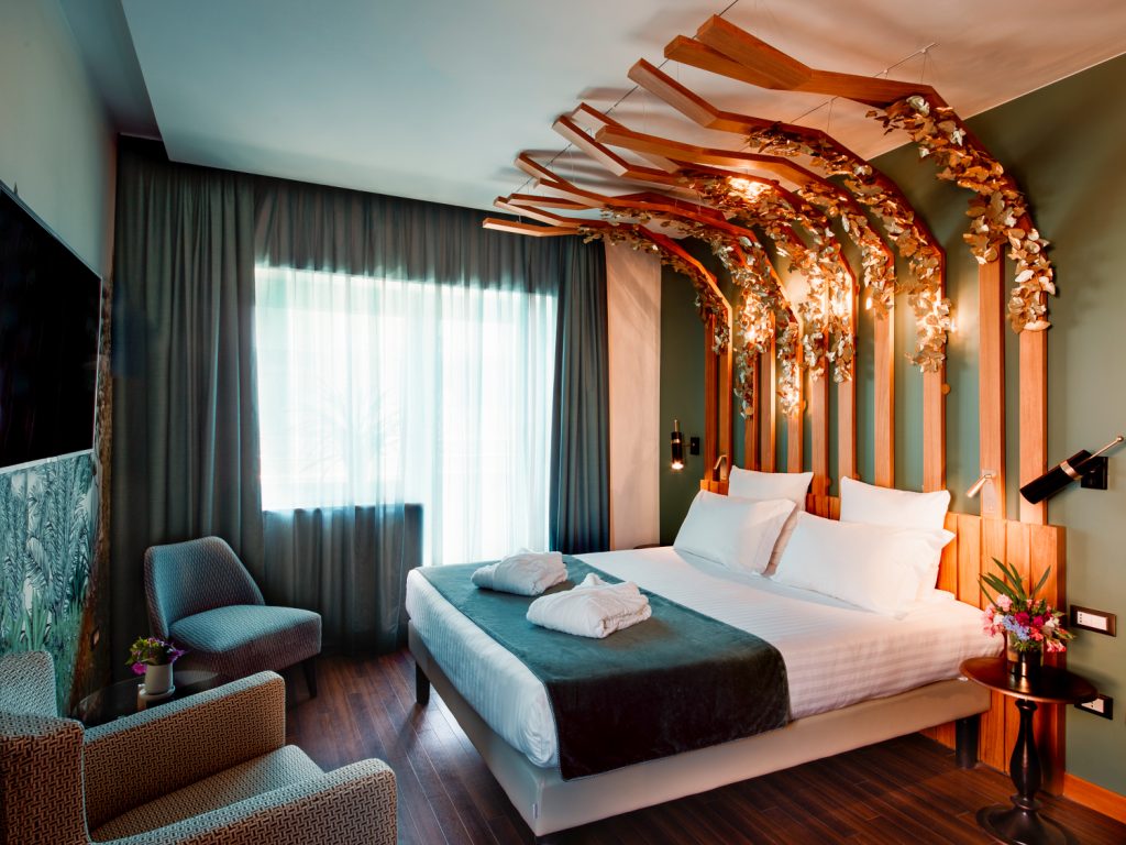Hotelzimmer des Mercure Roma Corso Trieste mit dunkelgrünen Akzenten und Doppelbett unter Vertäfelung mit goldenen Blättern