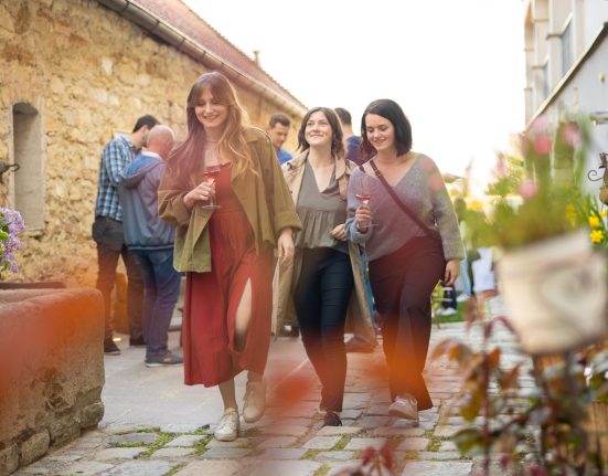drei Frauen spazieren lachend mit Weinglas