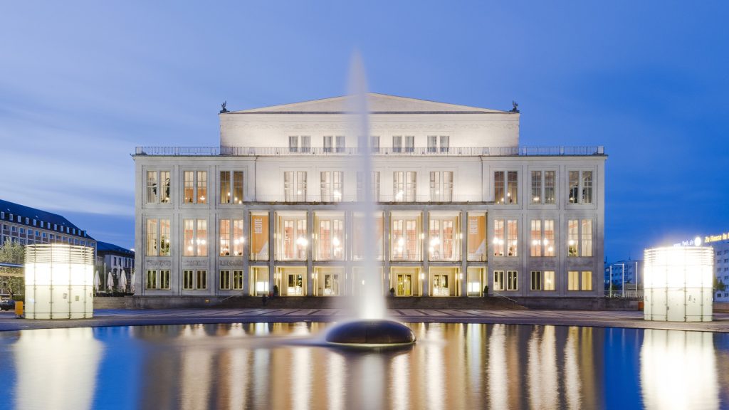 Die beleuchtete Oper Leipzig bei Dämmerung vor einem Springbrunnen
