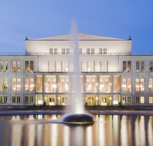 Die beleuchtete Oper Leipzig bei Dämmerung vor einem Springbrunnen