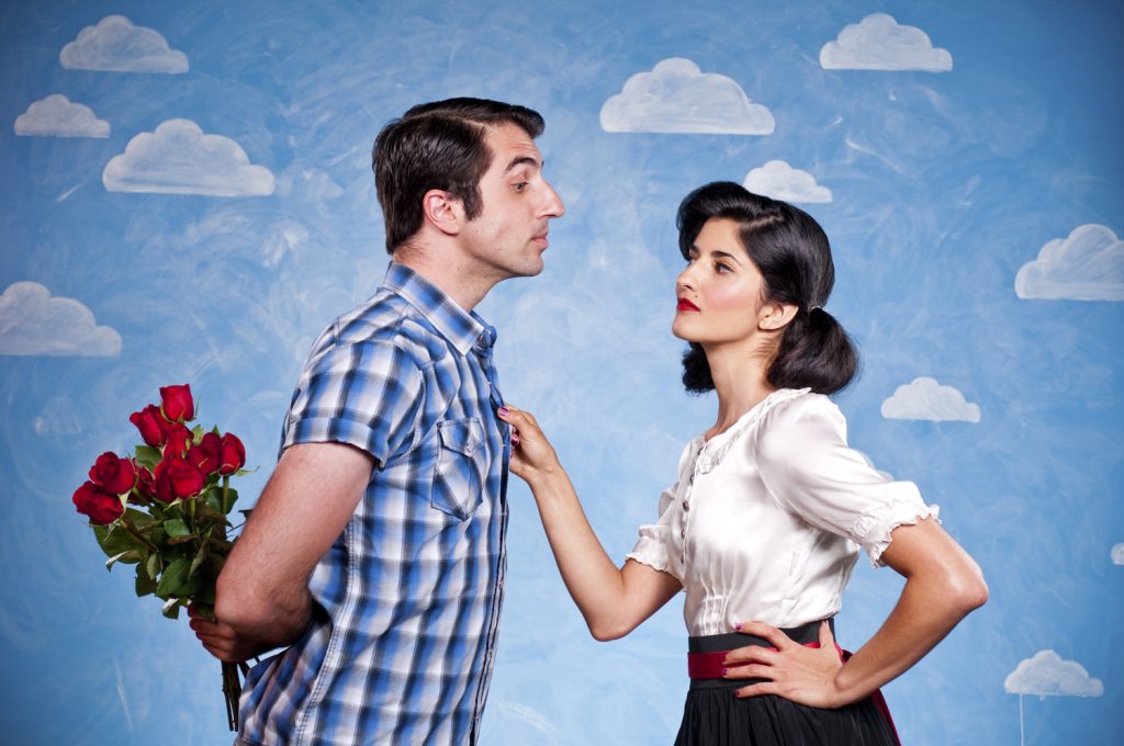 Mann mit roten Rosen steht einer Frau gegenüber, beide stehen vor einem blauen Hintergrund mit aufgemalten Wolken