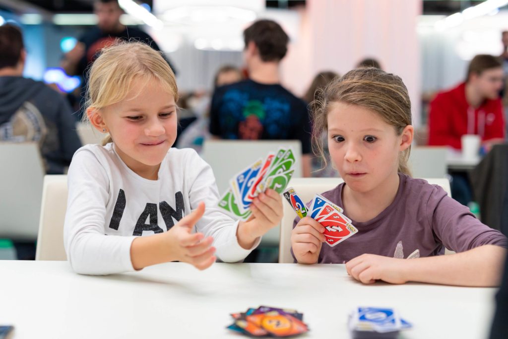 Zwei Kinder sitzen auf einem Tisch und spielen das Kartenspiel UNO.