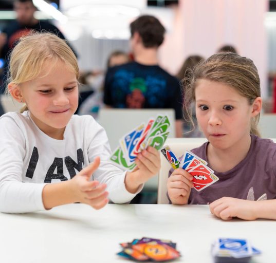 Zwei Kinder sitzen auf einem Tisch und spielen das Kartenspiel UNO.
