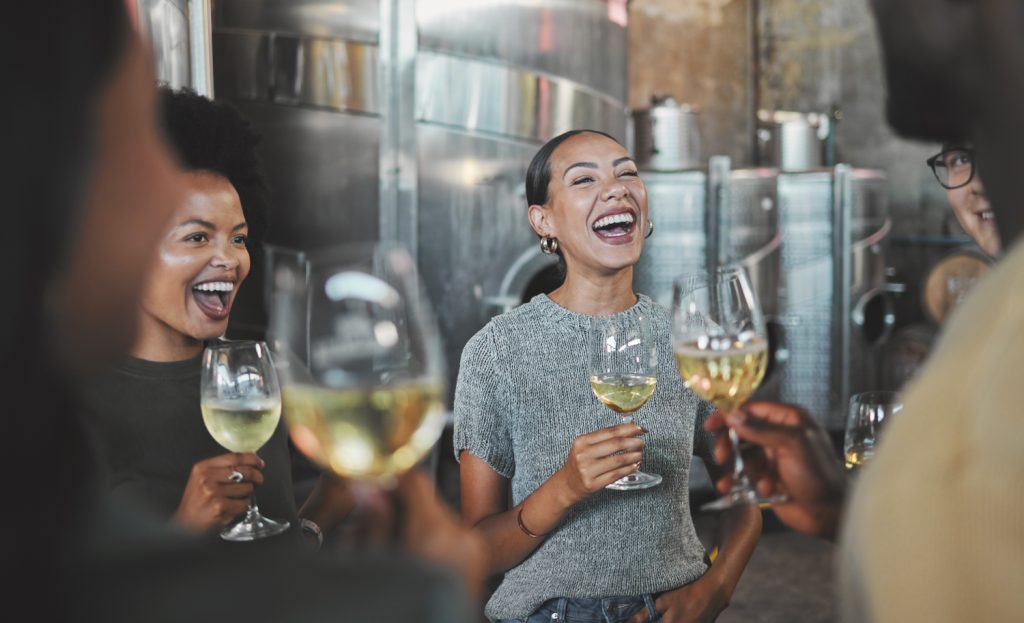 4 Personen sind mit einem Glas Wein in der Hand am lachen