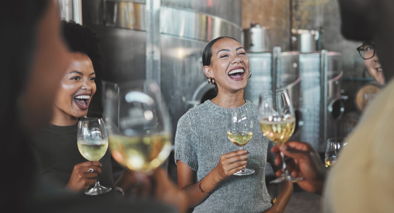 4 Personen sind mit einem Glas Wein in der Hand am lachen