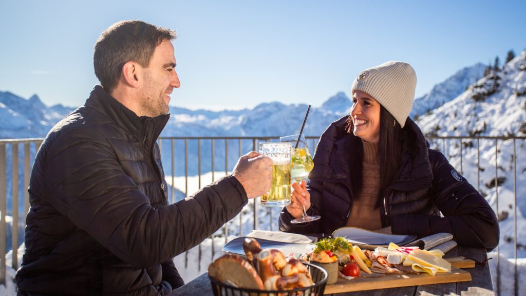 Paar bei ausgiebigem Frühstück im Bergrestaurant Jenneralm in Berchtesgaden auf 1.800 Metern, umgeben von verschneiter Berglandschaft