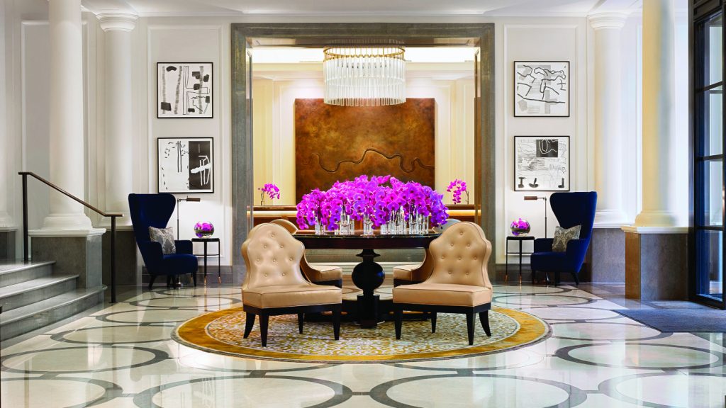 Lobby des Hotel Corinthia in London mit zwei breiten Ledersesseln, pinkfarbenen Blumensträußen und gigantischen Lustern