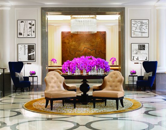 Lobby des Hotel Corinthia in London mit zwei breiten Ledersesseln, pinkfarbenen Blumensträußen und gigantischen Lustern