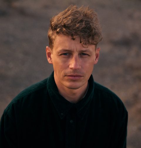 Ein Portraitfoto von einem Mann in einer Wüstenlandschaft.