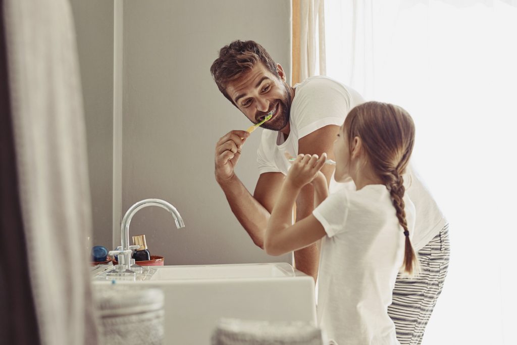 Vater und Tochter stehen vor dem Waschbecken und putzen sich die Zähne