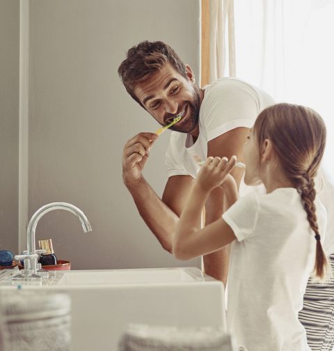 Vater und Tochter stehen vor dem Waschbecken und putzen sich die Zähne