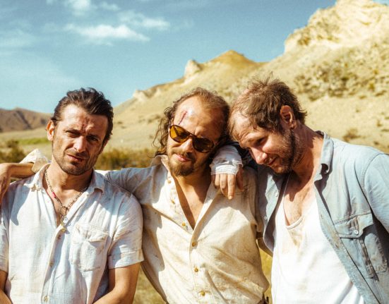 Drei Männer stehen in einer Wüste.