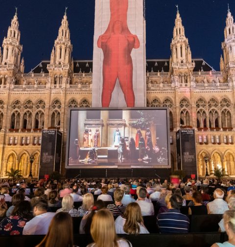 Menschenmenge sitzt vor dem Wiener Rathaus und sieht sich einen Film auf einer großen Leinwand an