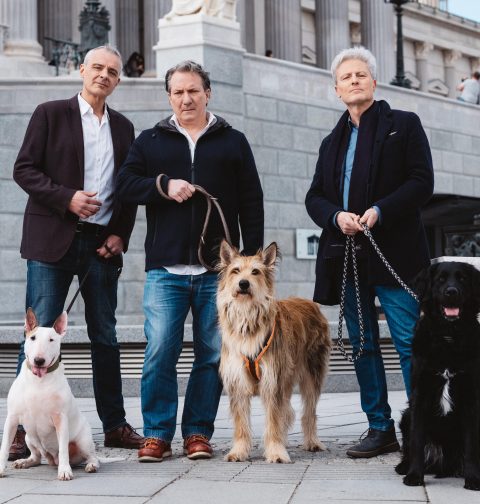 Die drei Kabarettisten stehen vor dem Wiener Parlament mit Hunden an der Leine.